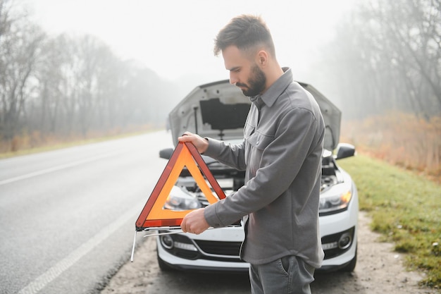 Homme triste sur la route à côté de la voiture cassée