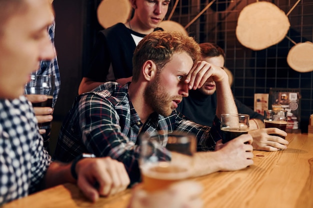 Un homme triste se sent mal Un groupe de personnes ensemble à l'intérieur du pub s'amuse le week-end