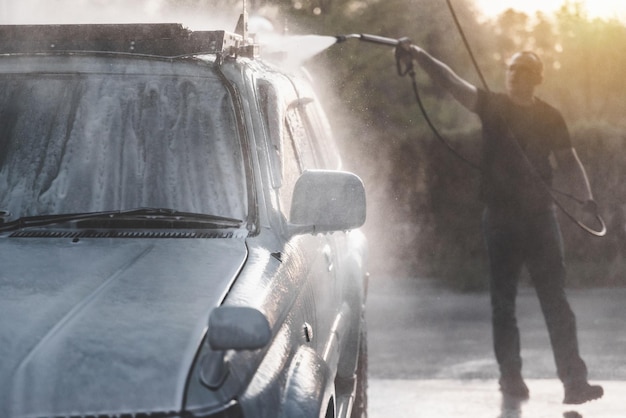 Photo un homme avec un tuyau à haute pression lave la mousse avec de l'eau dans un lave-auto libre-service