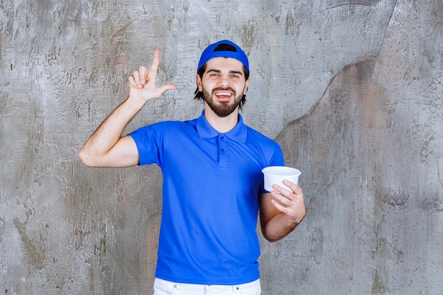 Homme en uniforme bleu tenant un gobelet en plastique à emporter et a l'air pensif