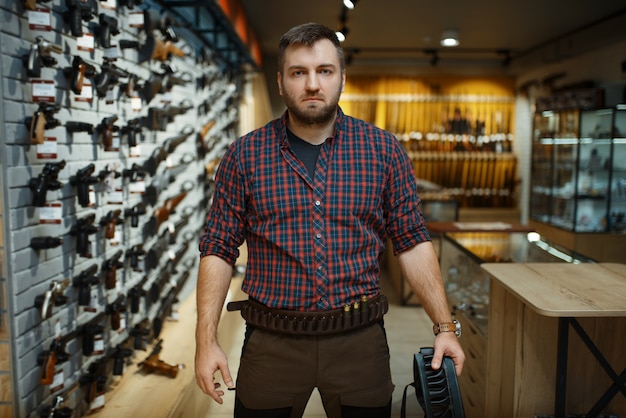 L'homme en uniforme de chasse détient une ceinture de munitions dans un magasin d'armes