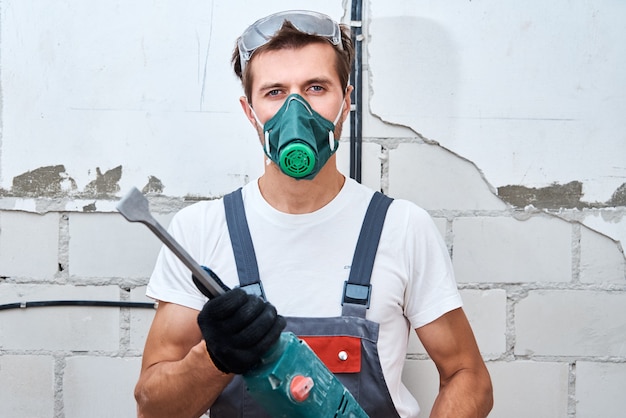 L'homme en uniforme de constructeur avec un marteau perforateur effectue des réparations dans la pièce. Concept de rénovation