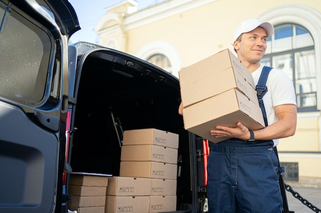 Un homme en uniforme est un employé d'une entreprise de messagerie qui livre des boîtes sur commande à un client