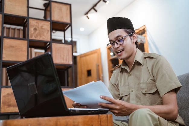 Homme en uniforme gouvernemental tenant des papiers tout en travaillant à domicile en ligne à l'aide d'un ordinateur portable