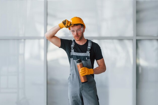 Un homme en uniforme gris près de la construction prend une pause à l'intérieur dans un grand bureau moderne pendant la journée