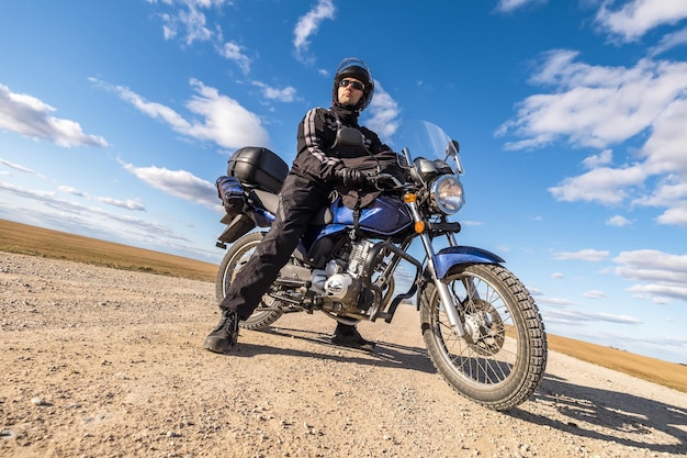 Homme en uniforme noir à vélo sur fond de panorama de champ et de ciel bleu concept de voyage en moto