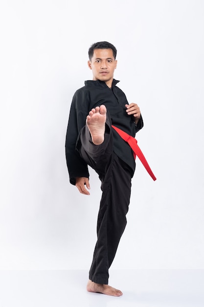 L'homme en uniforme de pencak silat fait un coup de pied en avant avec une jambe