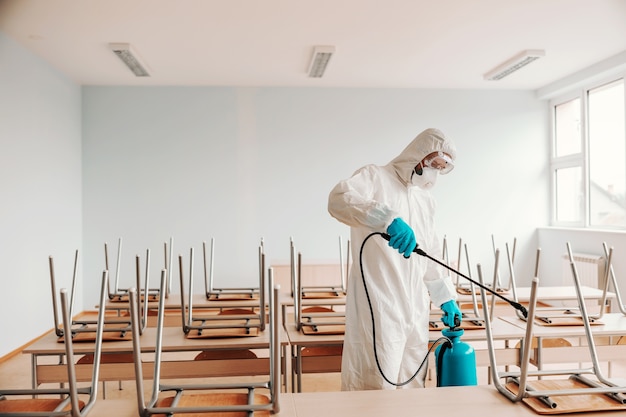 Homme en uniforme stérile, avec des gants et un masque tenant le pulvérisateur et la pulvérisation