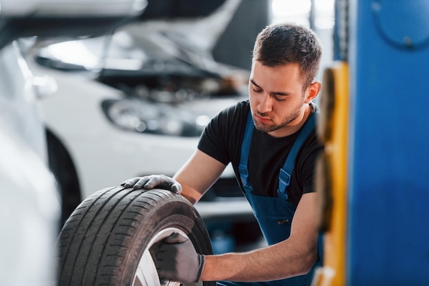 Homme en uniforme de travail assis et changeant de roue de voiture à l'intérieur Conception de service automobile