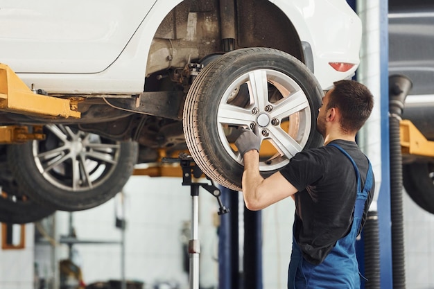 Homme en uniforme de travail changeant de roue de voiture à l'intérieur Conception de service automobile