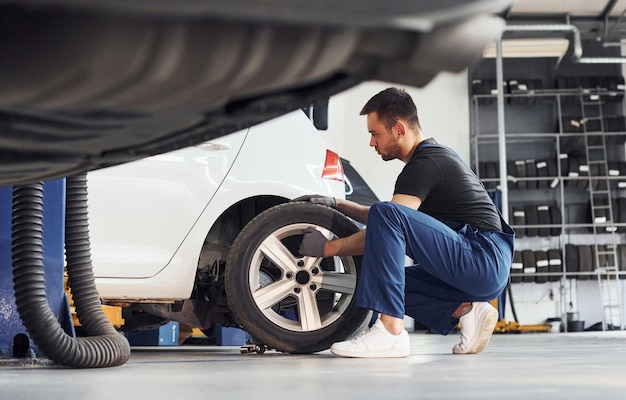 L'homme en uniforme de travail répare la voiture à l'intérieur Conception du service automobile