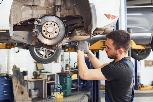 L'homme en uniforme de travail répare la voiture à l'intérieur Conception du service automobile