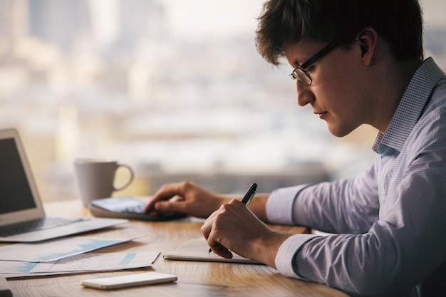 Homme utilisant une calculatrice et écrivant