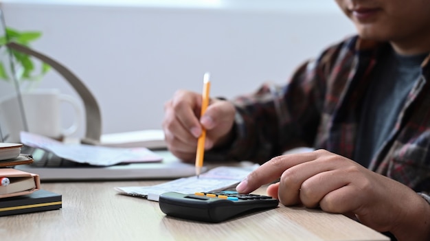 Homme utilisant une calculatrice pour calculer les factures à la maison.