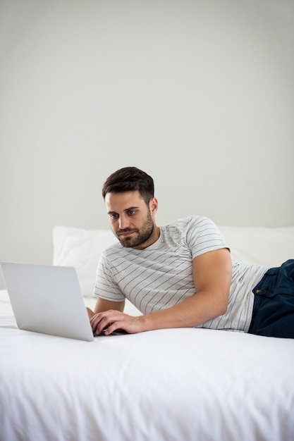 Homme utilisant un ordinateur portable sur le lit dans la chambre