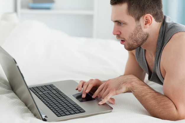 Homme utilisant un ordinateur portable en position couchée sur son ventre