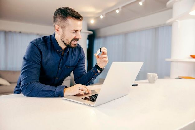 Un homme utilisant sa carte de crédit pour faire des achats en ligne sur l'ordinateur portable de sa maison confortable