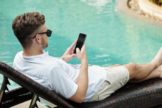 Homme utilisant un smartphone à la piscine extérieure