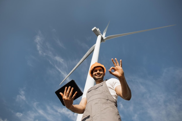 Homme utilisant une tablette et montrant le pouce vers le haut près des éoliennes