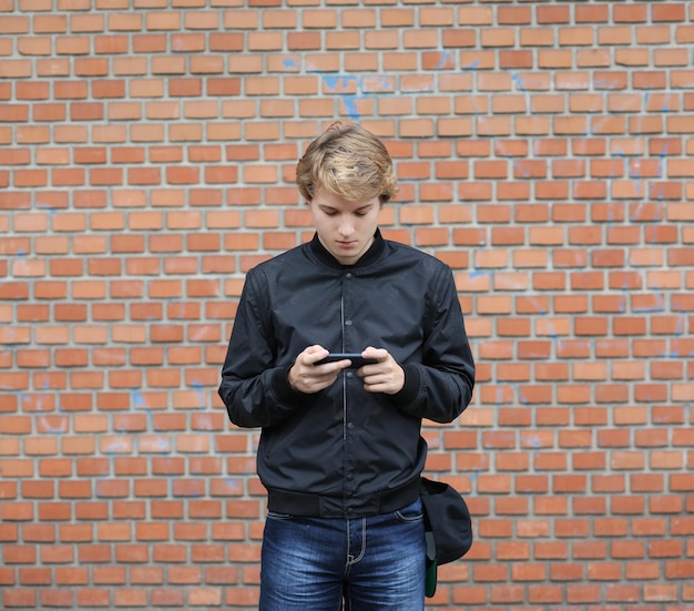 Homme utilisant un téléphone intelligent Adolescent debout près d'un mur de briques