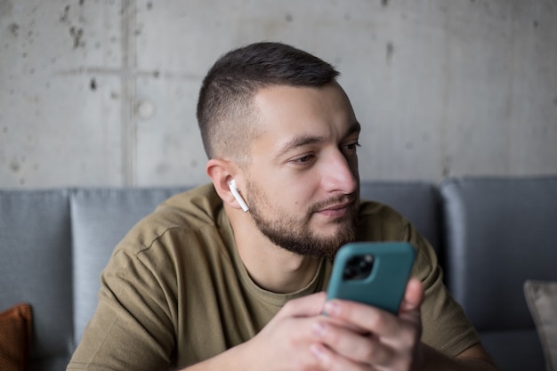 homme utilisant un téléphone portable et appréciant des chansons dans des écouteurs sans fil au café