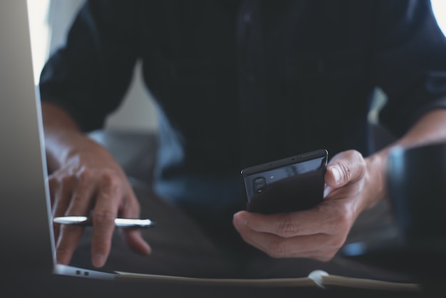 homme utilisant un téléphone portable et travaillant sur un ordinateur portable au bureau à domicile