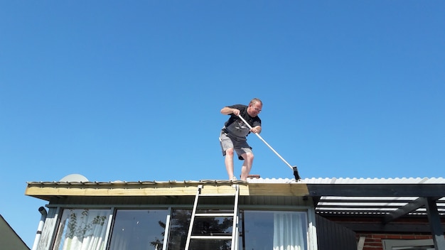 L&#39;homme utilise un balai pour nettoyer le toit de la maison.