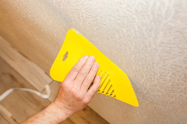 L'homme utilise un grattoir pour installer du papier peint. Nivellement du mur. Travaux de réparation d'entretien rénovation dans l'appartement. Restauration à l'intérieur.