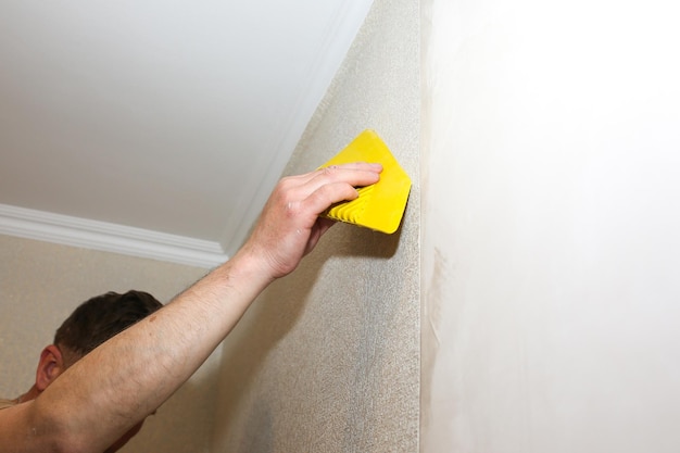 L'homme utilise un grattoir pour installer du papier peint. Nivellement du mur. Travaux de réparation d'entretien rénovation dans l'appartement. Restauration à l'intérieur.