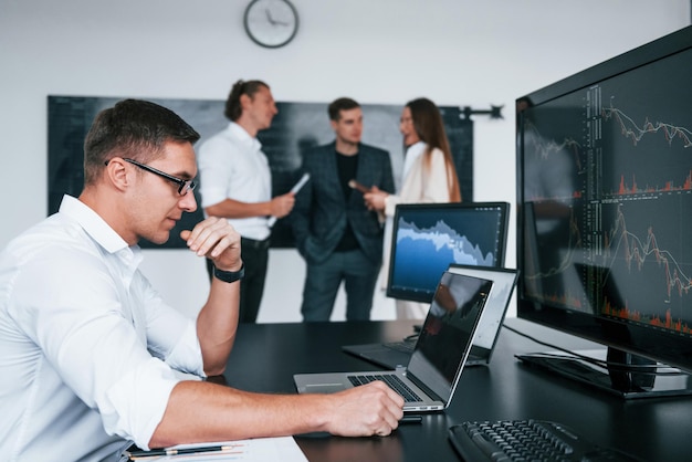 L'homme utilise un ordinateur portable Une équipe d'agents de change travaille dans un bureau moderne avec de nombreux écrans d'affichage