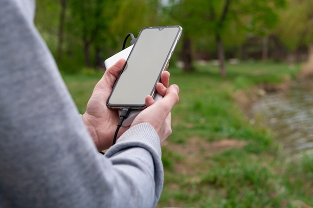 L'homme utilise un smartphone tout en chargeant à partir de la banque d'alimentation au bord des rivières