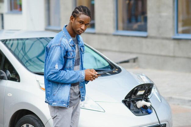 L'homme utilise un téléphone intelligent en attendant et l'alimentation se connecte aux véhicules électriques pour charger la batterie dans la voiture