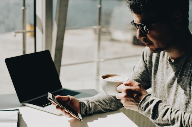 Photo un homme utilise un téléphone portable tout en buvant du café dans une tasse.