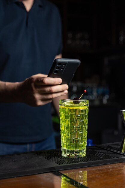 Un homme utilise un téléphone pour prendre un verre avec un liquide vert en arrière-plan