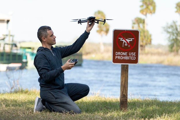 L'homme va piloter son quadcopter dans une zone interdite aux drones. L'opérateur utilise illégalement son drone dans un parc d'État près du panneau de restriction.