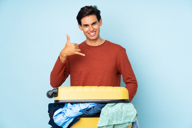 Homme avec une valise pleine de vêtements faisant un geste de téléphone