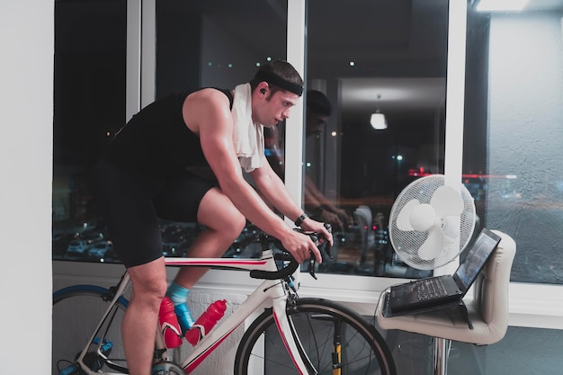 Homme à vélo sur l'entraîneur de machine il fait de l'exercice à la maison la nuit en jouant au jeu de course en ligne à vélo