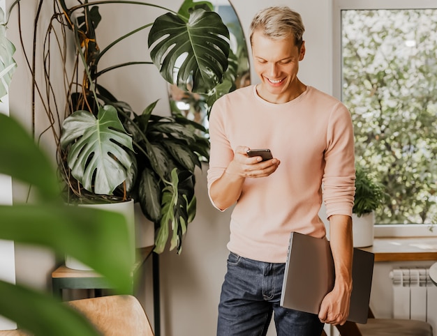 L'homme vérifie le téléphone, homme d'affaires avec ordinateur portable dans l'espace de travail dans un café écologique avec des plantes