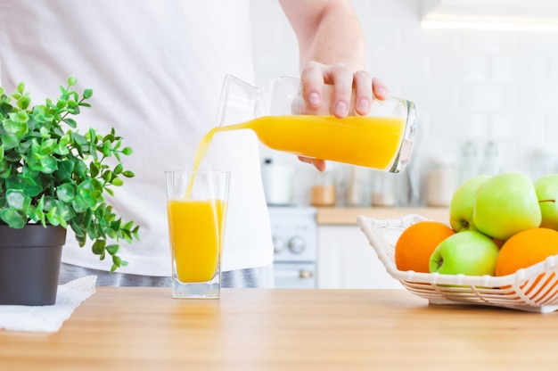 Photo homme versant le jus d'orange de la cruche dans un verre dans la cuisine.