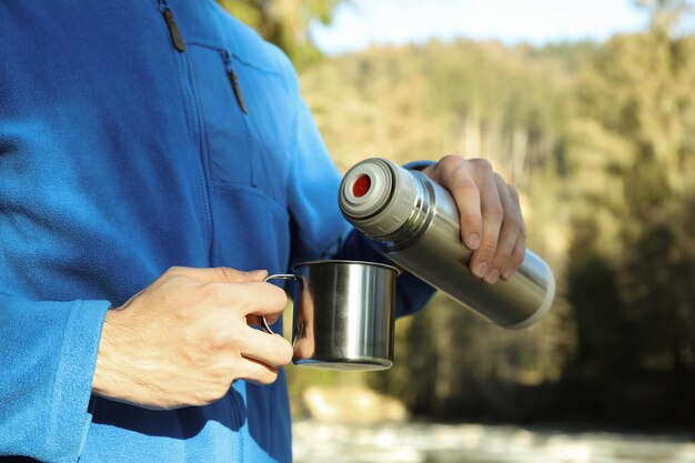 L'homme verse une boisson du thermos à la tasse en plein air