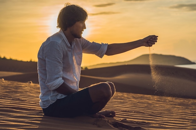 Un homme verse du sable dans le désert. Poncez entre les doigts du concept.