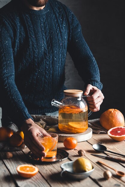 Un homme verse du thé aux agrumes sur une table en bois. Boisson saine, style vintage. Produits végétaliens et écologiques.