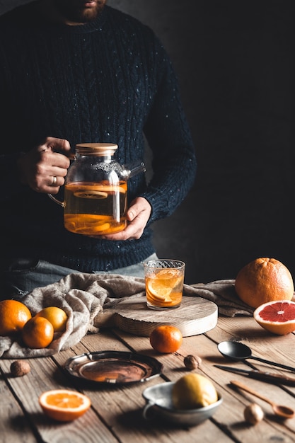 Un homme verse du thé aux agrumes sur une table en bois. Boisson saine, style vintage. Produits végétaliens et écologiques.