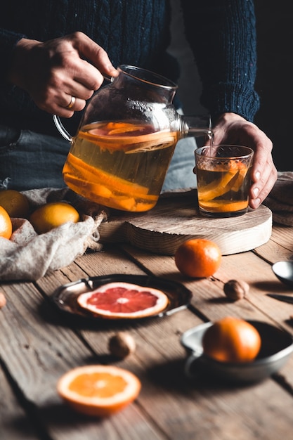 Un homme verse du thé aux agrumes sur une table en bois. Boisson saine, style vintage.