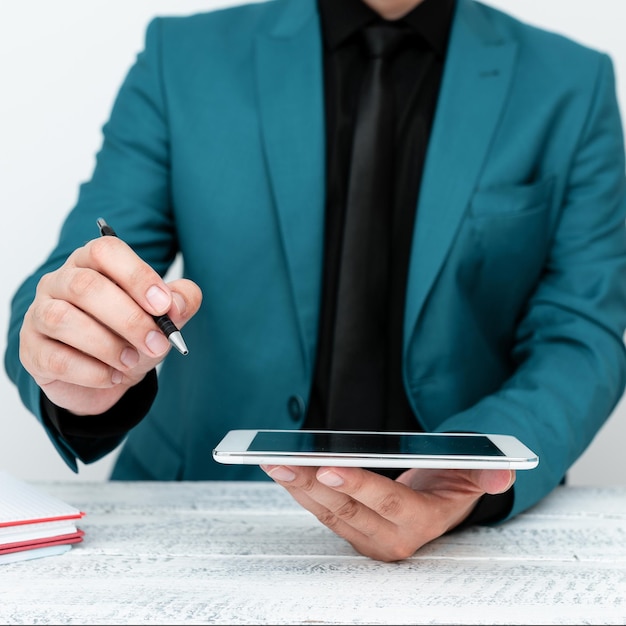 Homme en veste bleue assis à une table blanche et pointant avec un stylo sur un message important tenant un téléphone portable Monsieur montrant une annonce critique