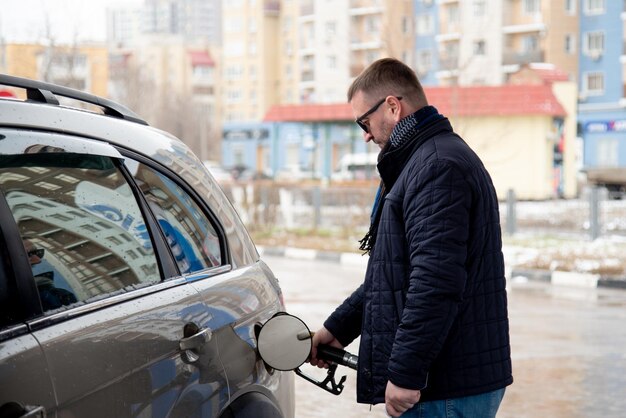 Un homme avec une veste bleue et des lunettes noires dans une station-service Il remplit la voiture Essence Lifestile