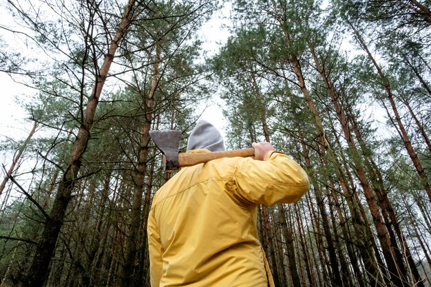 Homme en veste jaune en forêt avec hache