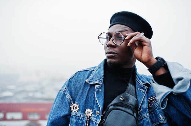 Homme en veste jeans, béret et lunettes posés sur le toit abandonné.