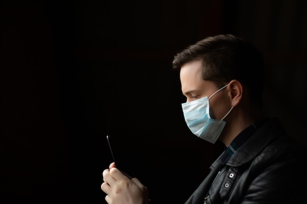 homme en veste noire avec masque facial à l'aide d'un téléphone mobile.