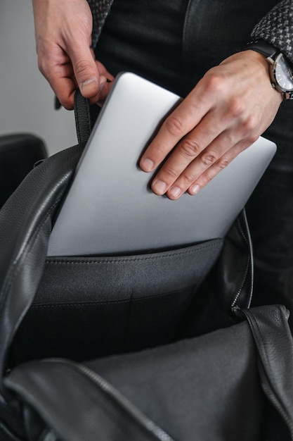 Un homme en veste pose sa main sur un ordinateur portable gris dans un élégant sac à dos en cuir noir